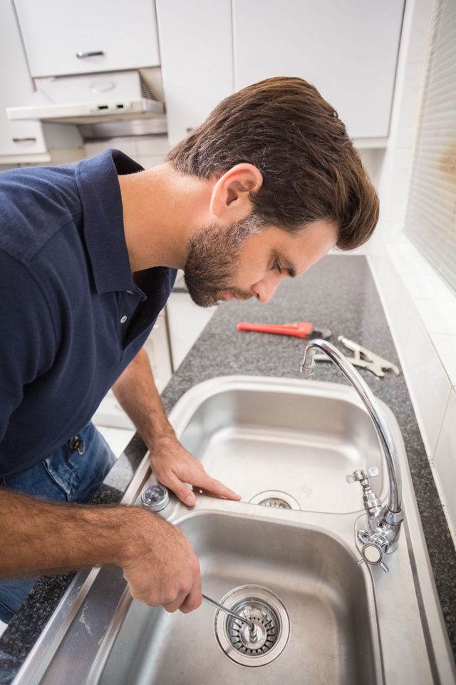 Plumber performing drain maintenance on a stainless steel kitchen sink